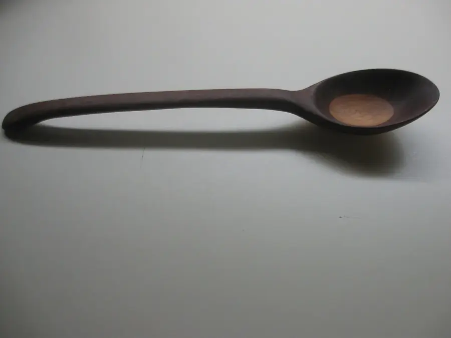 A single carved wooden spoon with a long handle lying on a pale surface
