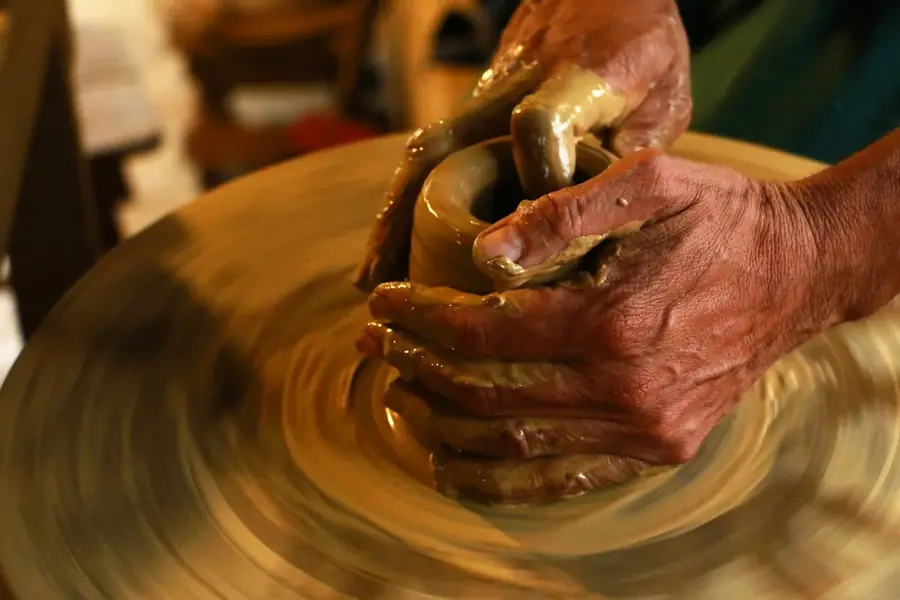 Hands shaping wet clay on a spinning potter's wheel