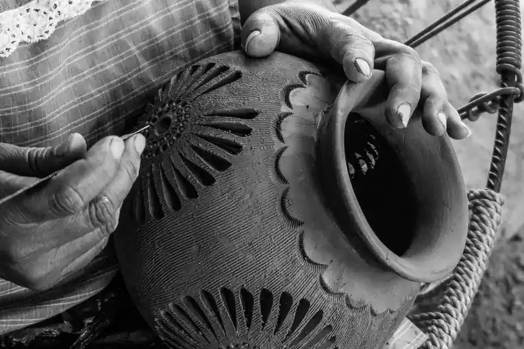 Black and white photograph of hands working a pattern into a round clay pot