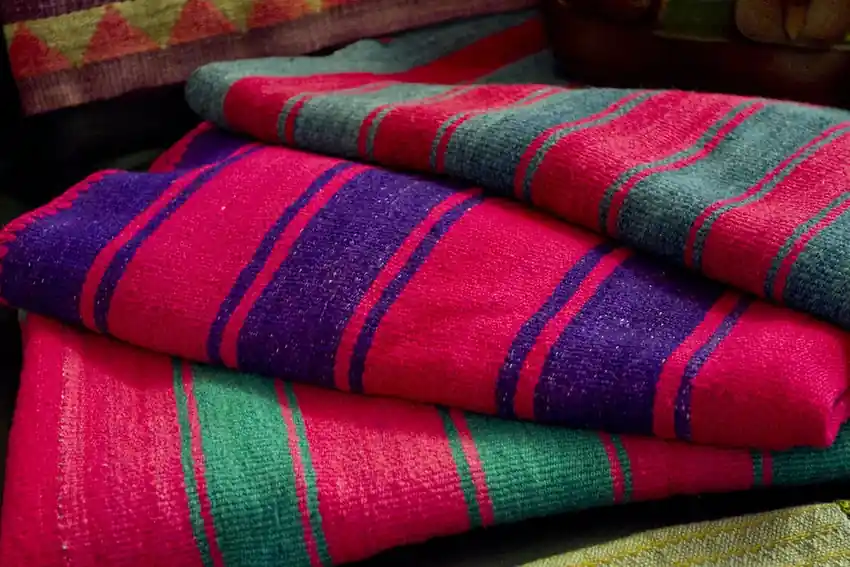 Folded hand-woven blankets striped in crimson, violet and green